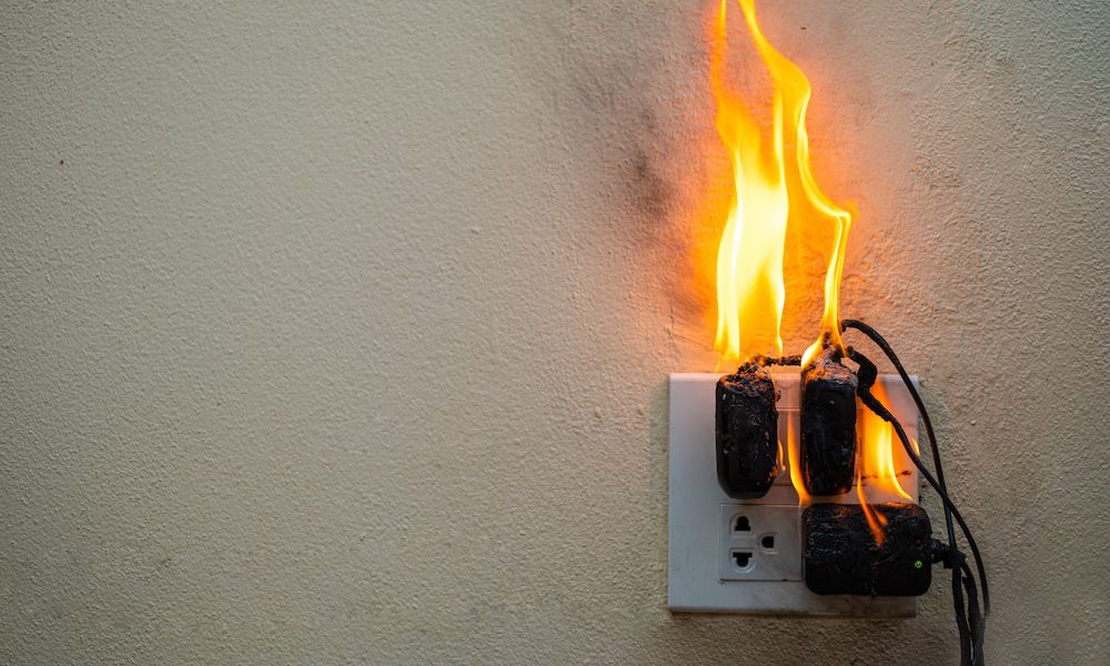 The Importance of Unplugging Electronics/ Safeguarding Your Home from Electrical Fires - outlet on a wall with 3 chargers plugged in on fire